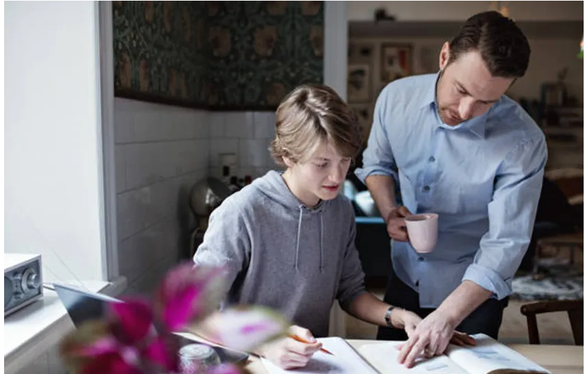A father helping his teenage son with schoolwork at home